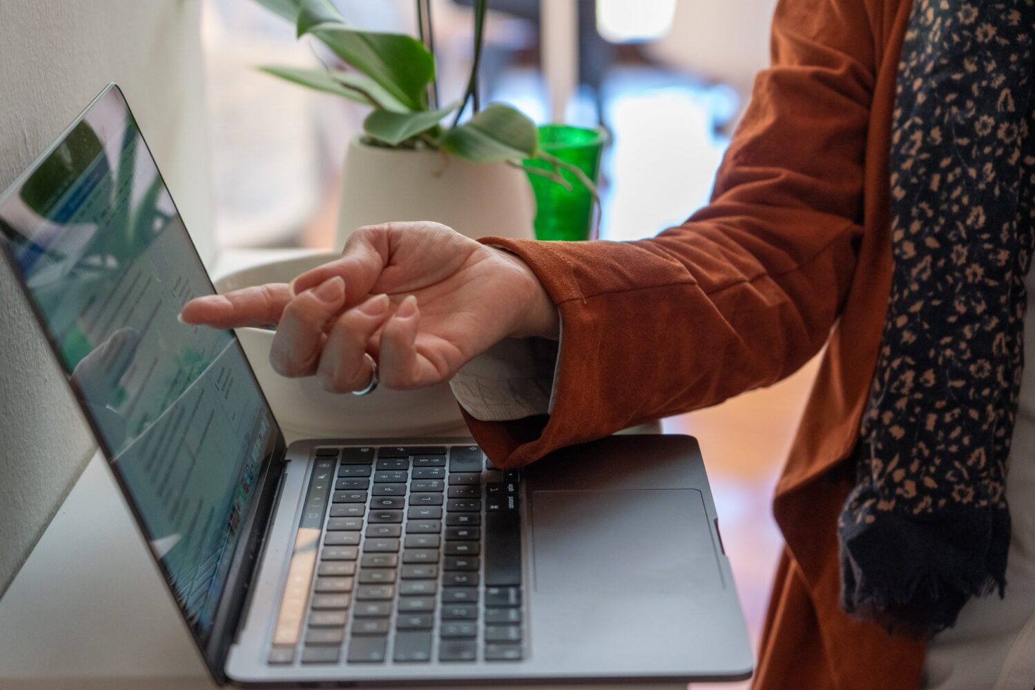 Una persona utilizza un laptop, indicando con la mano illo schermo, in un ambiente luminoso e moderno con piante.