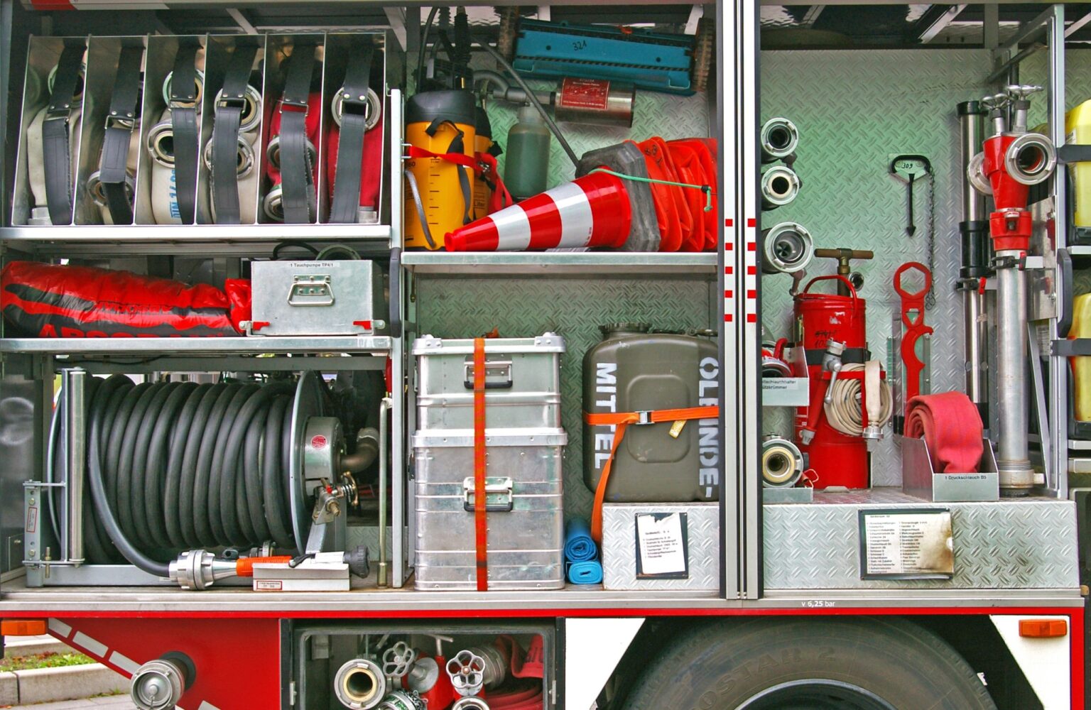Dettagli dell'interno di un camion dei pompieri, mostrando attrezzature come tubi, estintori e strumenti di emergenza organizzati in scomparti.