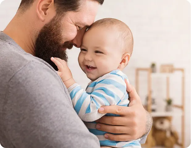 Un padre sorridente abbraccia il suo bambino, entrambi felici, in un ambiente accogliente e luminoso.